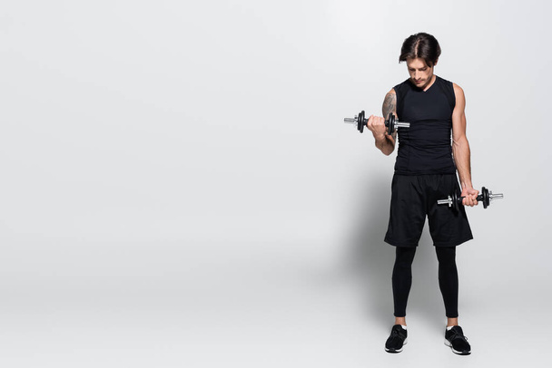 Full length of sportsman training with dumbbells on grey background - Foto, afbeelding