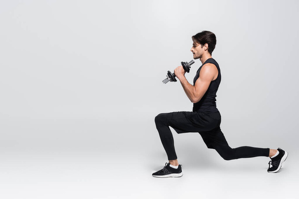 Side view of sportsman doing lunges and holding dumbbells on grey background  - Fotó, kép