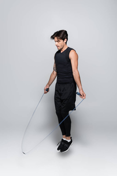 Sportsman jumping with rope on grey background  - Foto, Imagen