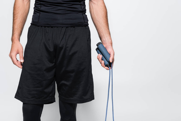 Cropped view of sportsman holding jump rope isolated on grey  - Foto, imagen