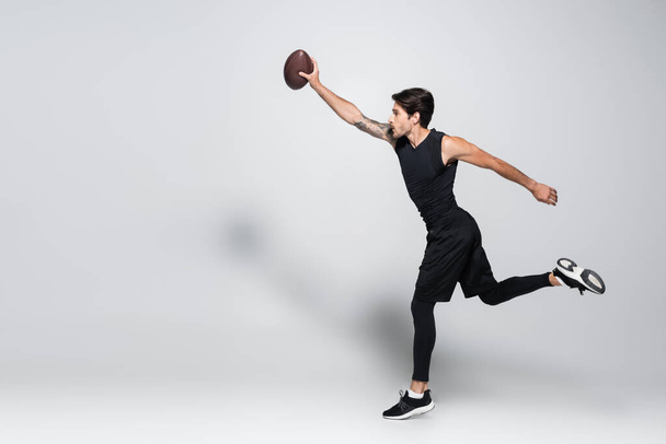 Side view of player with rugby ball running on grey background  - Photo, Image