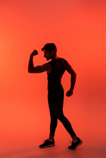 Urheilullinen urheilija näyttää lihaksia punaisella taustalla  - Valokuva, kuva