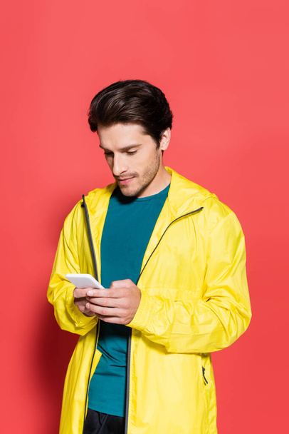 Спортсмен в спортивной куртке с помощью смартфона на красном фоне  - Фото, изображение