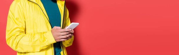 Обрезанный вид спортсмена с помощью мобильного телефона на красном фоне, баннер  - Фото, изображение