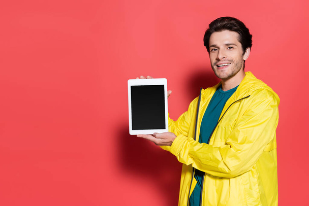 Positive sportsman holding digital tablet with blank screen on red background  - 写真・画像