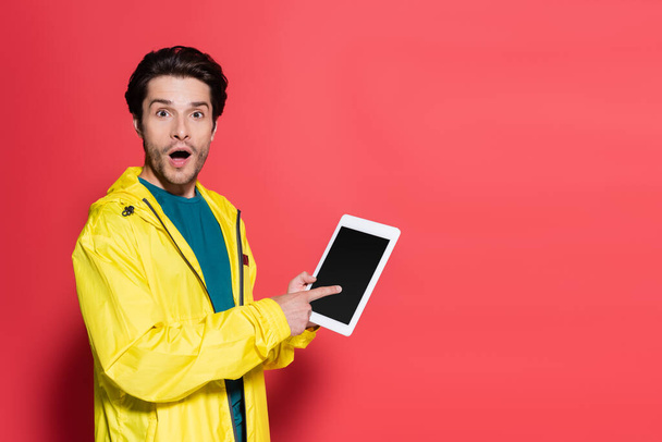Excited sportsman pointing at digital tablet with blank screen on red background  - Photo, Image