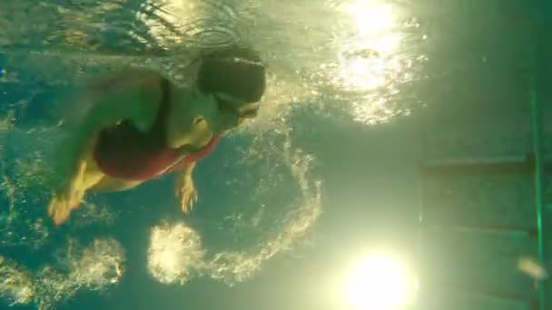 Młoda kobieta w czerwonym stroju kąpielowym pływa pod wodą - odpycha się stopami z boku i odwraca - Materiał filmowy, wideo