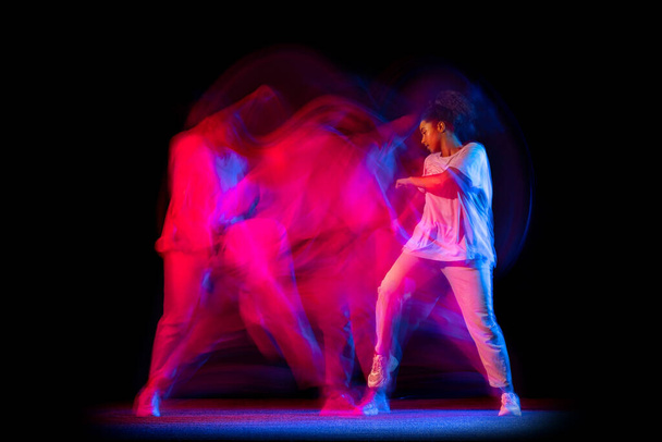 Sportive young girl in white costume dancing hip-hop dance isolated on dark background at dance hall in neon mixed light. - Foto, immagini