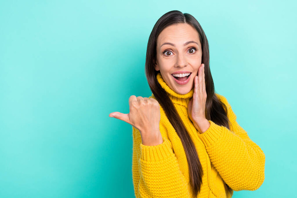 Photo of sweet excited woman wear yellow sweater arm cheek pointing empty space isolated turquoise color background - Fotoğraf, Görsel