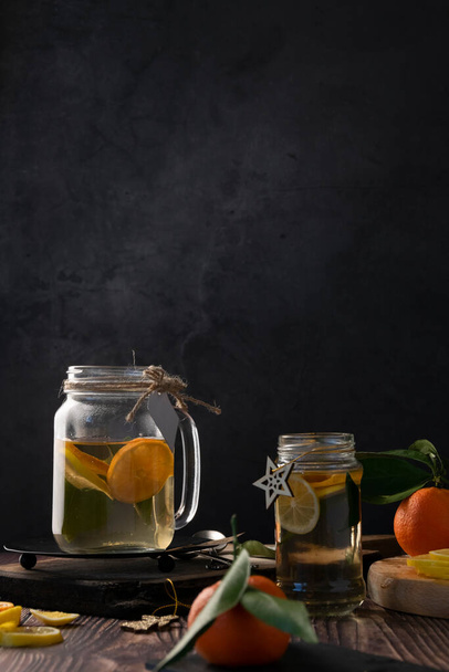 Theepot met warme citrusthee van sinaasappelen, citroenen en limoenen, gezonde drank, rustieke achtergrond - Foto, afbeelding