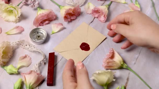 Ręce biorące wosk szczelną kopertę z marmurowego stołu w pobliżu różowych kwiatów zbliżyć  - Materiał filmowy, wideo