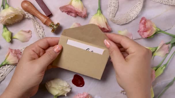 Руки открывают конверт с карточкой "Выходи за меня замуж" над мраморным столом рядом с розовыми цветами.  - Кадры, видео