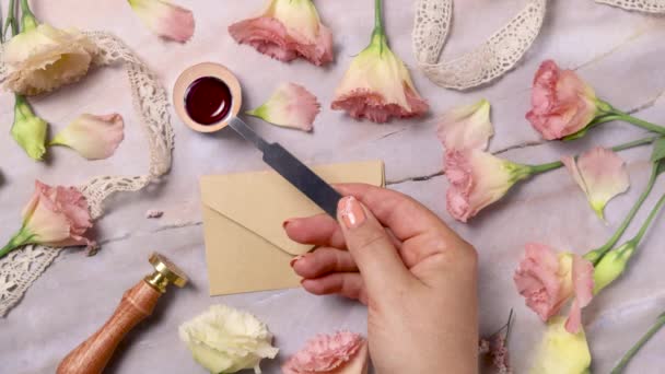 Ruce vylévající rozpuštěný vosk na obálku poblíž růžových květin na mramorovém stole zblízka  - Záběry, video