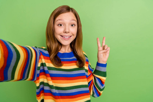 Self-portrait of attractive cheerful trendy red-haired girl showing v-sign isolated over bright green color background - Foto, Imagen