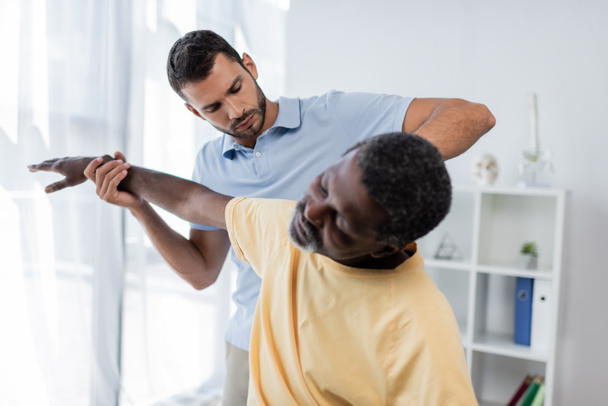 young doctor examining mature african american patient in rehabilitation center - Foto, Bild