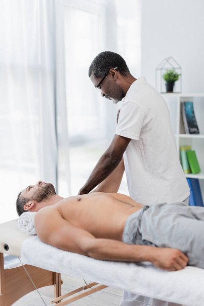 african american physical therapist massaging man in rehab center - Foto, Bild