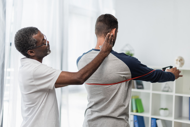 african american rehabilitation trainer assisting man working out with resistance band - Foto, immagini