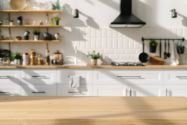 Scandinavian kitchen interior design with white furniture and diverse decorations. Wood stylish table in foreground. Household appliances. Bright dining room after repair - Foto, imagen