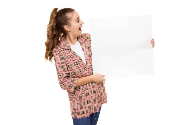 Fotografie krásné úžasné roztomilé roztomilé smějící se šťastný brunetka dospívající dívka s culíkem ve stylové kostkované bundě, bílé tričko a drží bílý prázdný list izolované na bílém pozadí s - Fotografie, Obrázek