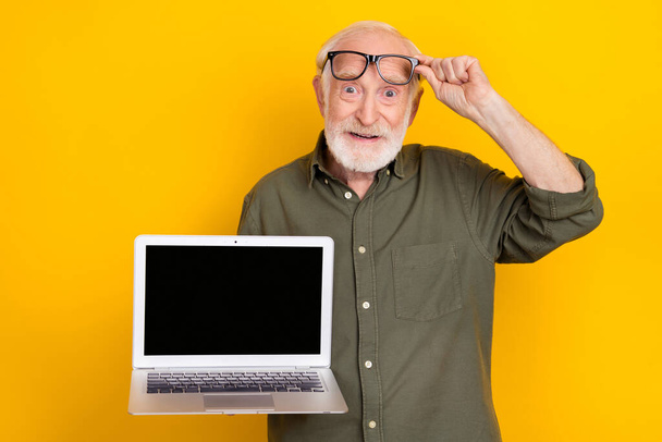 Portrait of satisfied positive person hold show empty space netbook display promo isolated on yellow color background - Foto, imagen