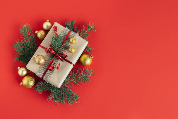 Craft gift box with spruce branch and christmas ornaments on a red background. Holiday concept. Place for text. Flat lay. - Φωτογραφία, εικόνα