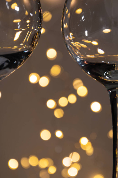 A background of bright bokeh lights, between the parts of two transparent glasses. Transparent wine glasses, partly in the frame and background - side of bright lights. - Valokuva, kuva