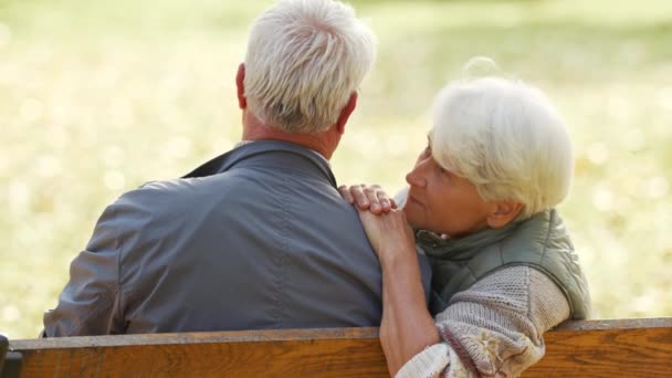 Ein älteres Ehepaar sitzt auf der Bank im Park. Frau stützt ihren Kopf auf Manns Schulter und streichelt seine Haare - Filmmaterial, Video