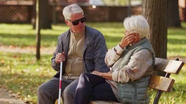 Blinde oudere man zit met zijn vrouw op de bank in het park en houdt een blinde stok vast. - Video