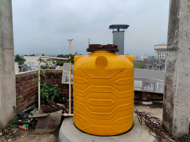 Photo de stock de vieux réservoir d'eau en plastique de couleur jaune sur le toit ou la terrasse du bâtiment résidentiel à Gulbarga, Karnataka, Inde.Photo prise pendant la journée de pluie, se concentrer sur l'objet. - Photo, image