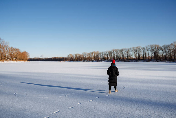 Panoramic view of the lake in winter. A young girl walks on a frozen lake. Bright cold sun. Nature walk in winter weather.footprints in the snow. High quality photo - Φωτογραφία, εικόνα