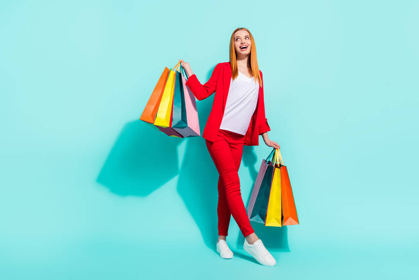 Photo of charming pretty orange hair woman dressed red jacket looking empty space holding bargains isolated cyan color background - Φωτογραφία, εικόνα