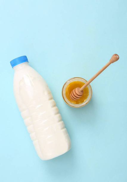 Milk bottle and honey on blue background - 写真・画像