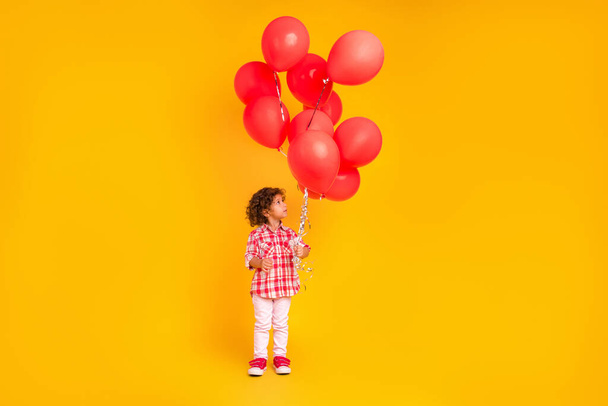 Photo of pretty dreamy school girl dressed checkered clothes holding red balloons smiling isolated yellow color background - Foto, Bild