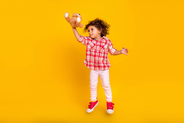 Photo of pretty sweet school girl dressed checkered clothes jumping holding toy looking empty space isolated yellow color background - Φωτογραφία, εικόνα