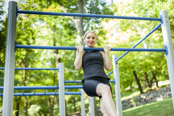 Mladá fit žena se vytáhne na vodorovnou tyč na cvičišti. Venkovní cvičení - Fotografie, Obrázek
