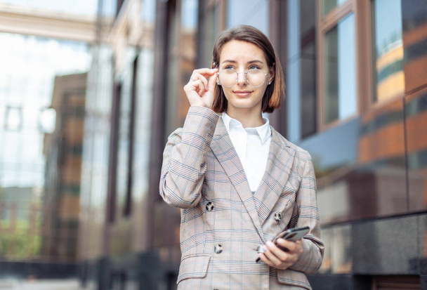 Business portrait of a young stylish confident modern woman in the city against the background of a business building - Photo, Image