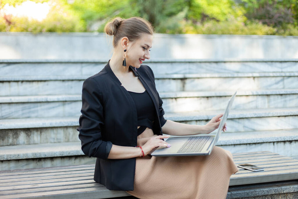Onnellinen liiketoiminnan nainen käyttää kannettavaa tietokonetta istuessaan penkillä puistossa - Valokuva, kuva