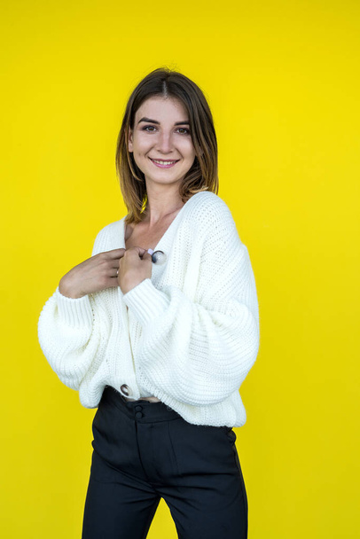 divat portré egy fiatal csinos lány pózol a kamera öltözött kötött fehér pulóver előtt egy sárga fal - Fotó, kép