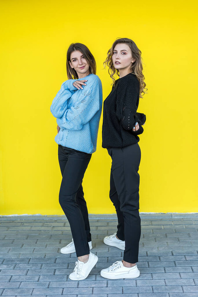 young girlfriends posing together in modern knitted sweaters isolated on yellow wall studio portrait - Photo, image