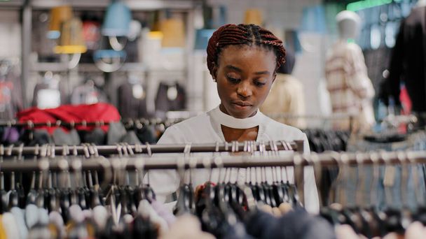 Μόνος χαρούμενος African American κορίτσι χιλιετή γυναίκα αγοραστής αγοραστής αγοραστής στέκεται στο κατάστημα ειδών ένδυσης εμπορικό κέντρο επιλέγοντας μοντέρνα φορέματα προϊόντα γυναικεία έκπτωση ψώνια πωλήσεις χαμηλές τιμές, έννοια της μόδας - Φωτογραφία, εικόνα
