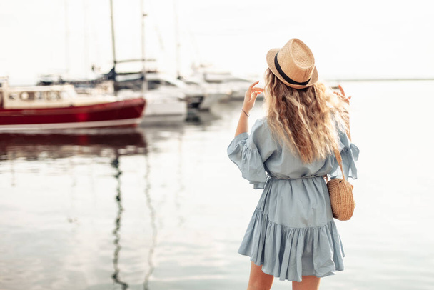 A cute young woman in a plaster and a hat looks at the yacht club - Foto, imagen