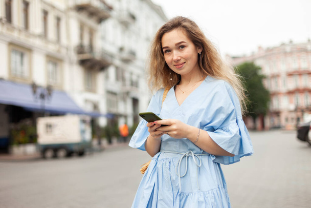 Jeune femme mignonne en robe en utilisant le téléphone en ville - Photo, image