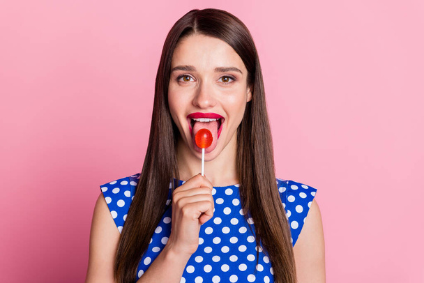 Photo of young attractive woman happy positive smile lick lollipop sugar sweet isolated over pink color background - Foto, immagini