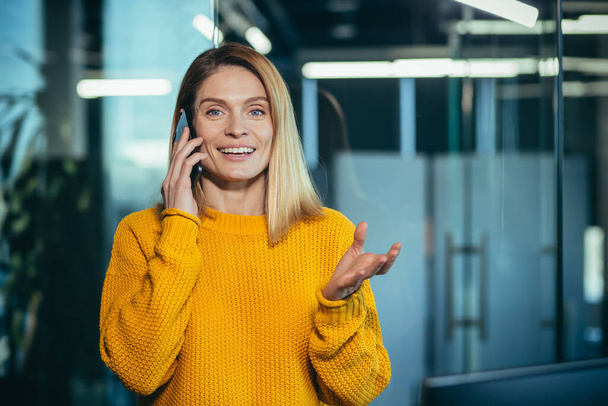 Successful freelancer woman talking on the phone rejoices, looks at camera and smiles, business woman boss in modern office - Foto, Bild