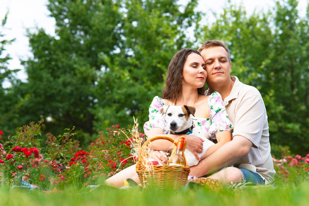 Famille romantique, jeune couple dans le jardin sur un pique-nique câlins. Femme et homme amoureux sur l'herbe avec leur chien Jack Russell Terrier - Photo, image