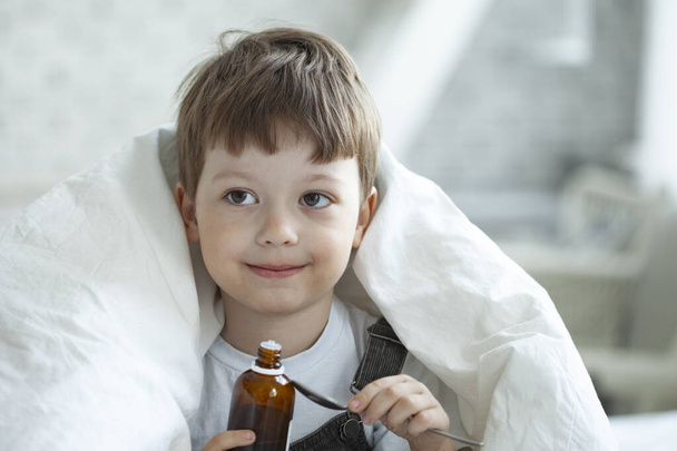 Sick child boy drinking cough syrup sitting on bed at home, children recover from flu. - Foto, Bild
