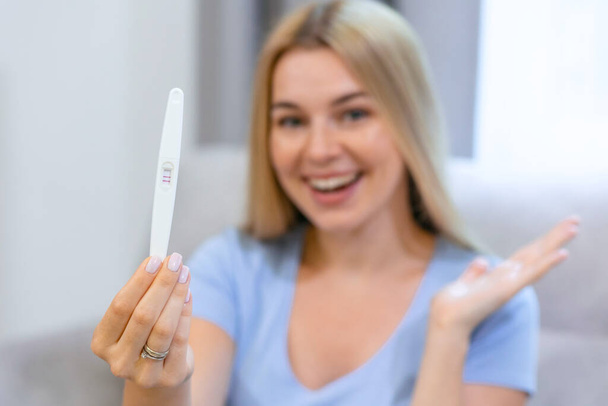 A beautiful woman takes a pregnancy test and as soon as she reads that she is pregnant, she explodes in a moment of happiness and joy for the future birth of her child. Concept of: birth, life, family - Photo, Image