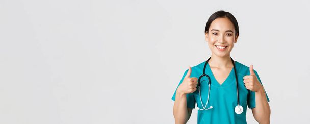 Healthcare workers, preventing virus, quarantine campaign concept. Close-up of upbeat smiling asian doctor, physician looking confident, ensure patient, showing thumbs-up in approval - Photo, Image
