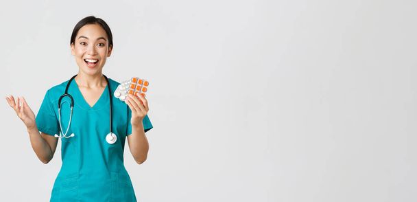 Egészségügyi dolgozók, vírusmegelőzés, karantén kampány koncepció. Izgatott boldog ázsiai női orvos, nővér orvosi maszk mutatja csodálatos új gyógyszert, ajánljuk gyógyszertár - Fotó, kép