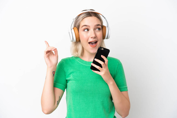 Joven mujer caucásica aislada sobre fondo blanco escuchando música con un móvil y cantando - Foto, imagen